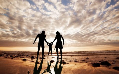 Happy family together hand in hand on the beach at sunset, summer time. Mother, father and a little child